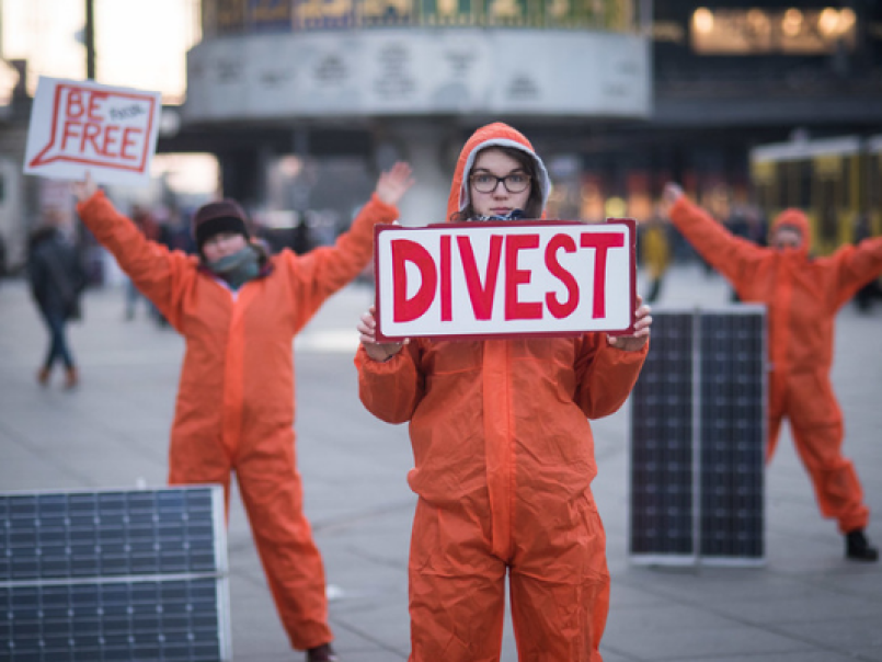 Picture of someone in a orange boiler suit holding up a divest sign