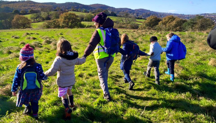 Woman and children all holding hands walking on a field with hills in distance