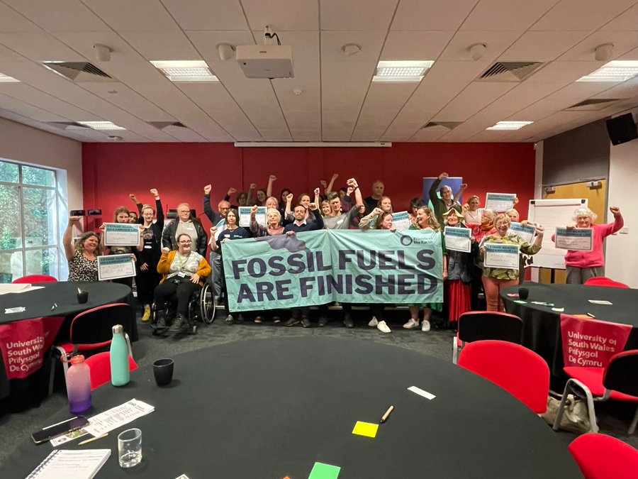 Group of people behind a banner, 'Fossil Fuels are Finished', with their hands in the air