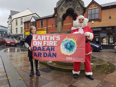 A child and someone in a Santa costume holding a Earth's on Fire placard