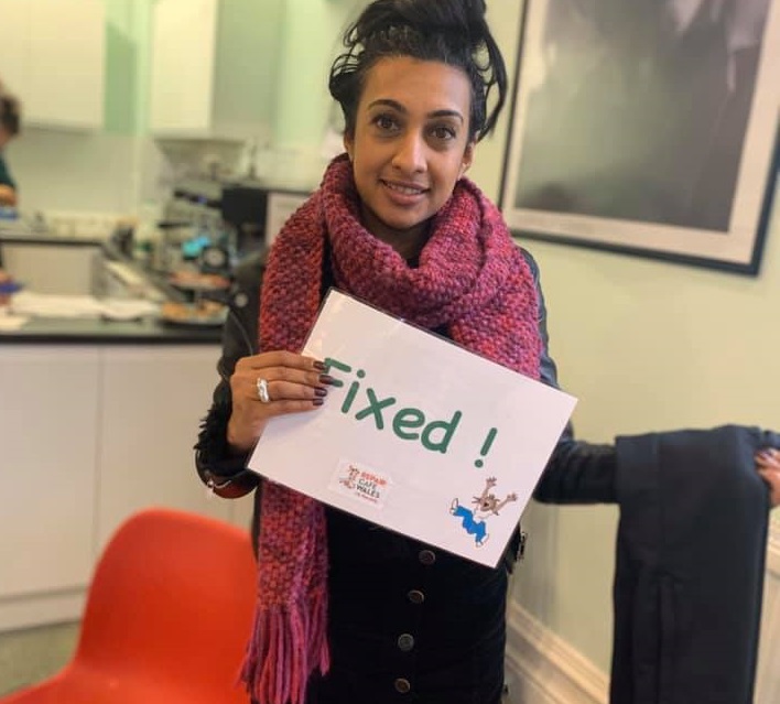 Photo of a woman in a repair cafe holding a pair of trousers with a 'fixed' sign