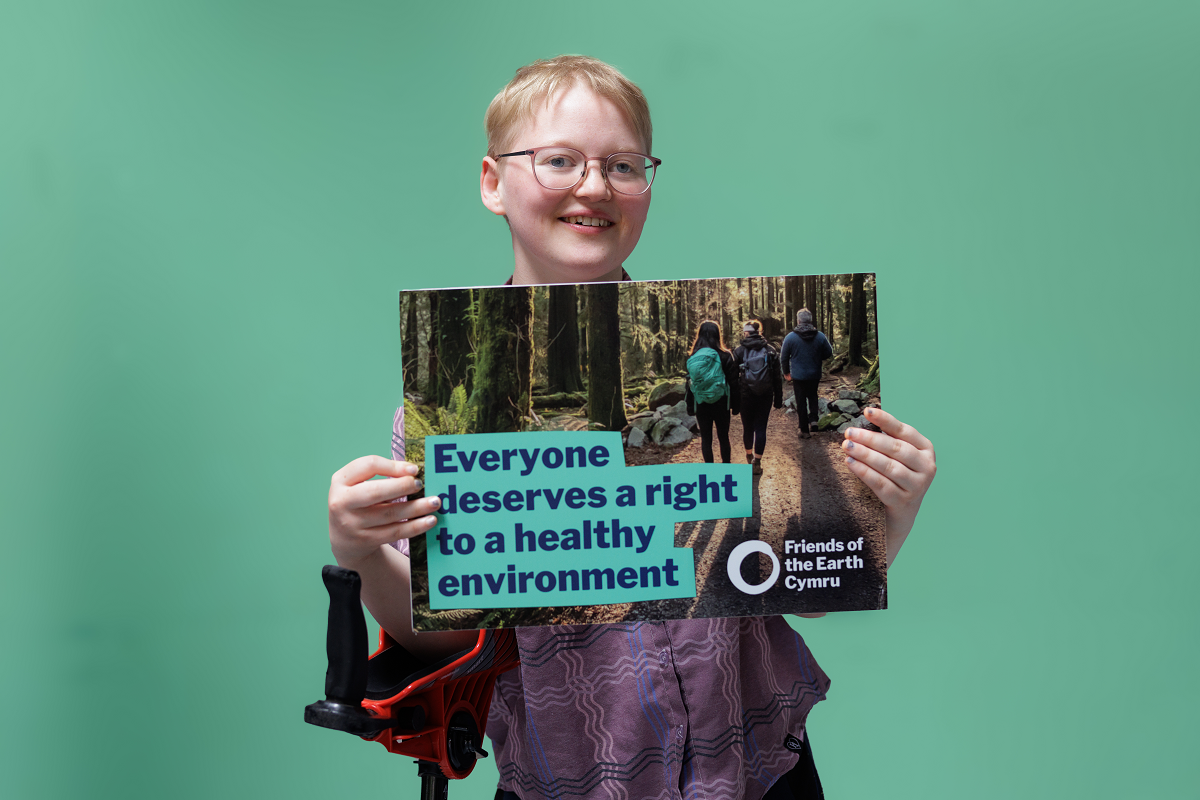 A young person with a walking stick, holding up a sign saying Everyone deserves a right to a healthy environment