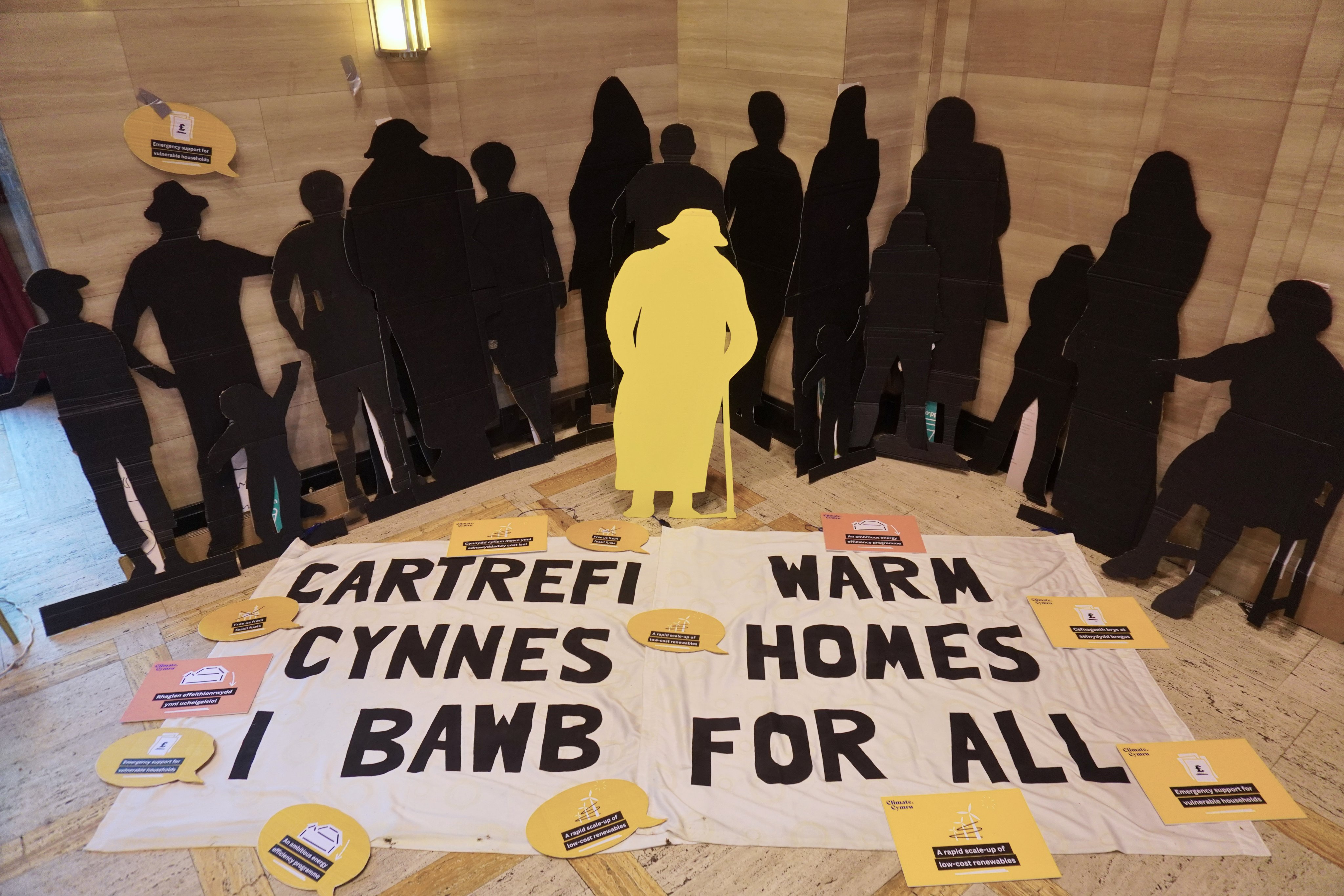 Life-sized back silhouettes behind a banner, 'warm homes for all'