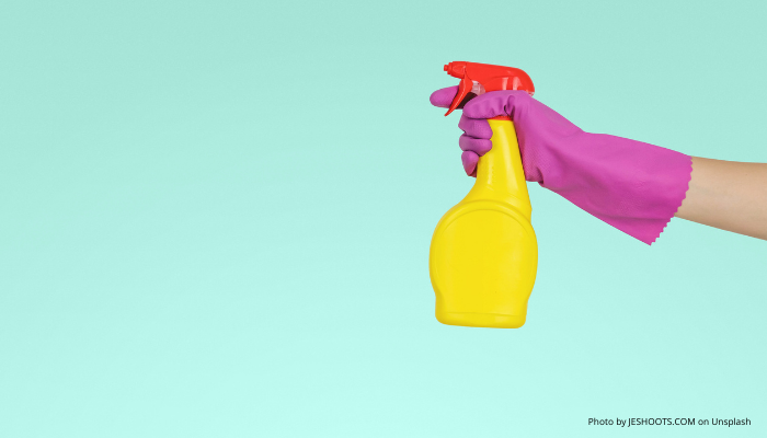 Hand squeezing a spray bottle wearing marigold gloves.