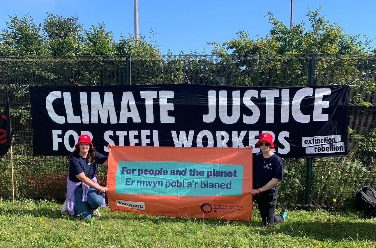 Two people holding a banner For People and the Planet behind a bigger banner Climate Justice for Steel Workers