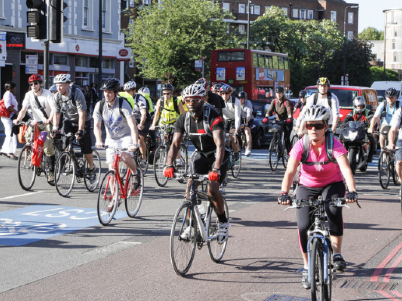 Lots of people cycling on a road with a bus in the background