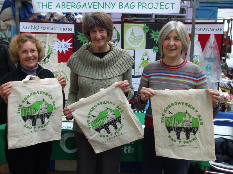 Three women in front of a stand holding and displaying canvas bags with the title 'The Abergavenny Bag'