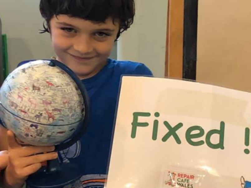 Boy at a repair cafe with a globe and a fixed sign