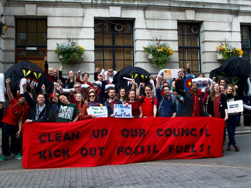 People protesting holding a banner 'Clean up our council - kick out fossil fuels/Pobl yn protestio yn dal baner 'Glanhau ein cyngor - cicio tanwydd ffosil''/