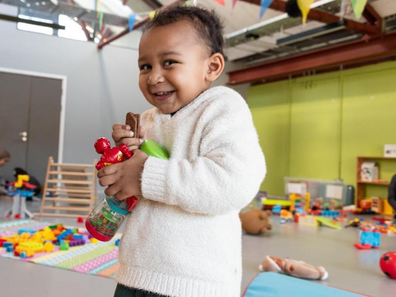 Child grasping a few toys and looking at the camera
