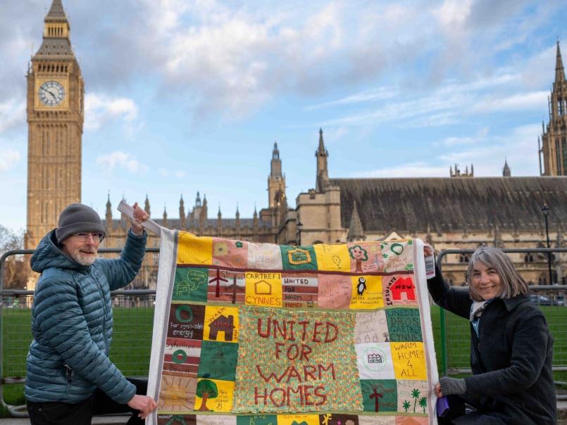 Two people holding up a quilt outside Westminster