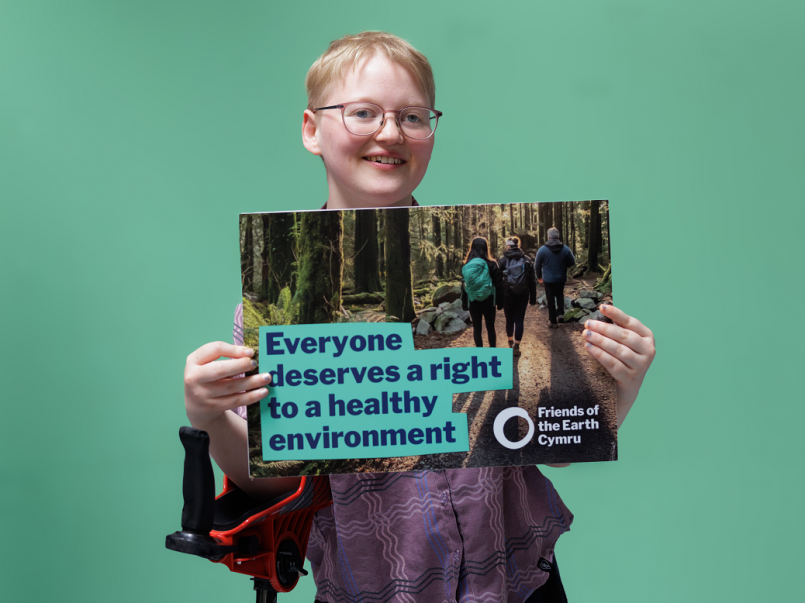 A young person with a walking stick, holding up a sign saying Everyone deserves a right to a healthy environment
