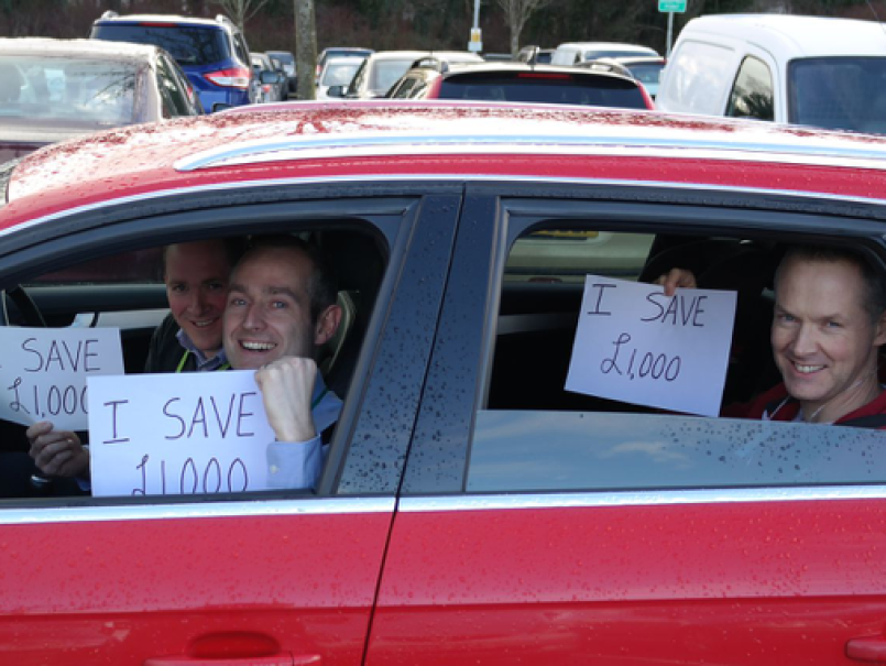 People in a car holding up a sign saying how much they are sharing by lift sharing