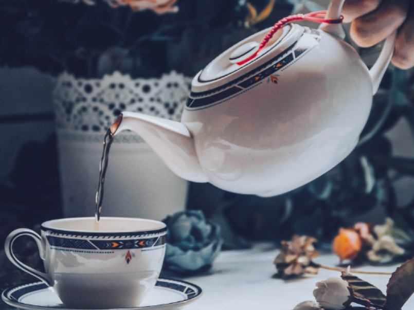 Someone pouring tea from a teapot into a cup with a saucer