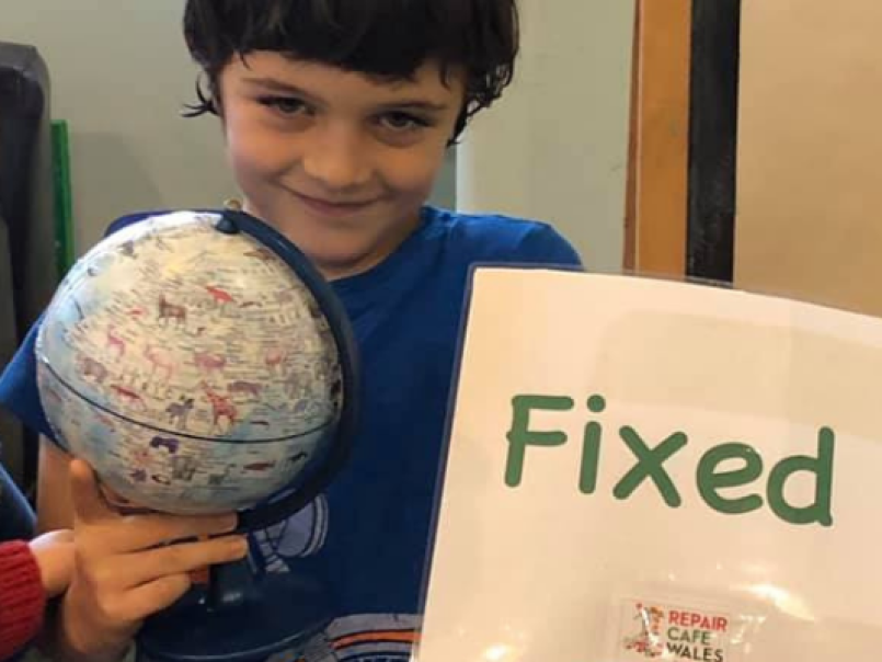 Boy in a repair cafe holding up a globe and a sign signing fixed
